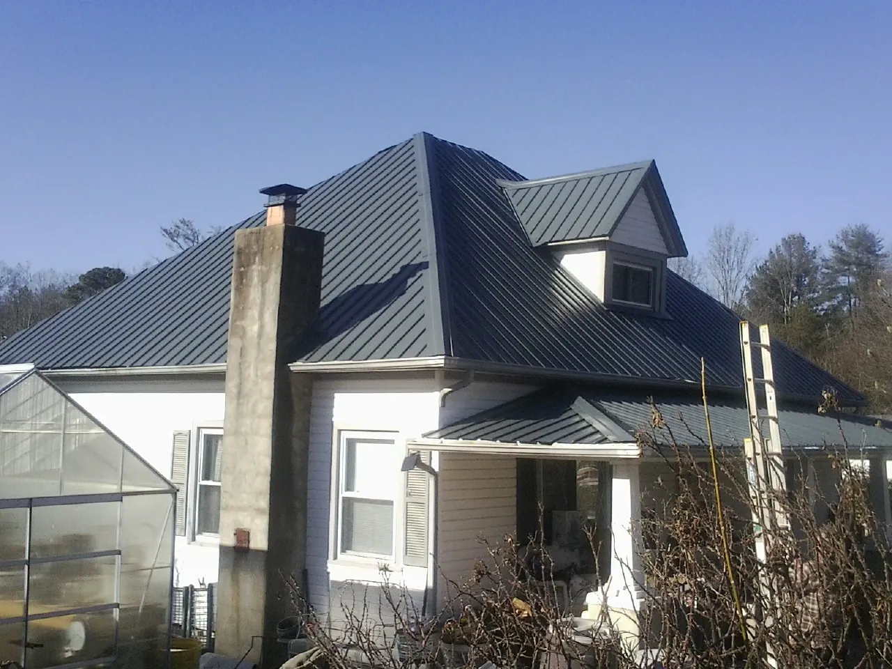 Dark blue standing seam metal roof on a white farmhouse with dormer — Slate & Tile Roof Repair by Roofing Brothers in Tennessee
