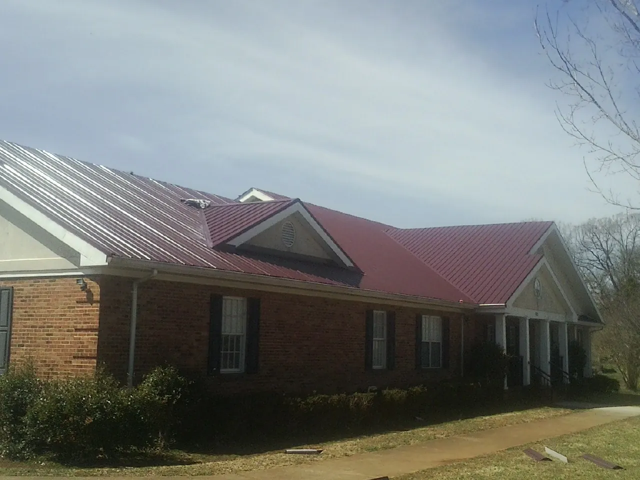 Red metal roof with gabled entries on a long brick building, from a Hail Damage Roof Repair job in Tennessee