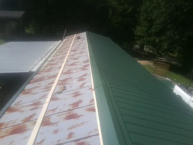Old rusted panels beside newly installed green metal roofing in Tennessee