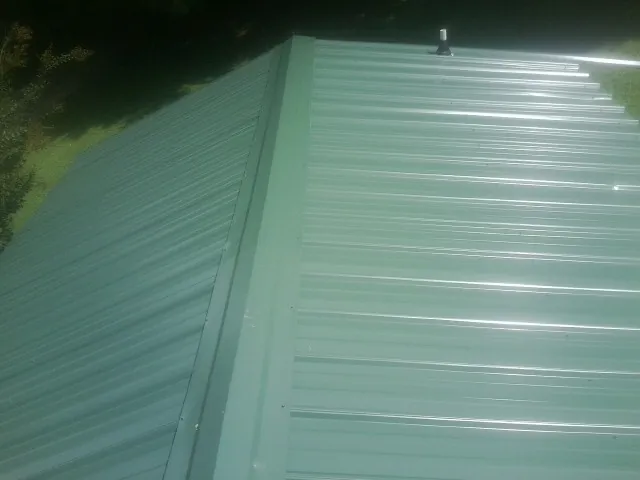New green metal panels meeting at the ridge of a roof — Flat Roof Repair work by our crew in Tennessee
