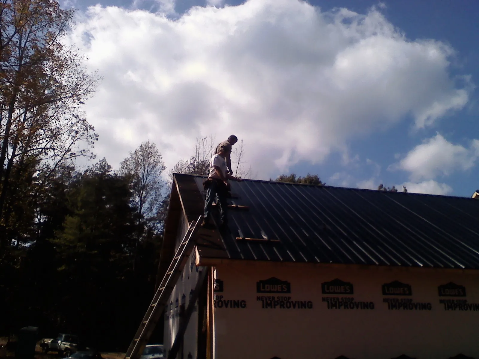 Roofer fastening dark metal panels high against a cloudy sky, from a Roof Inspection job in Tennessee