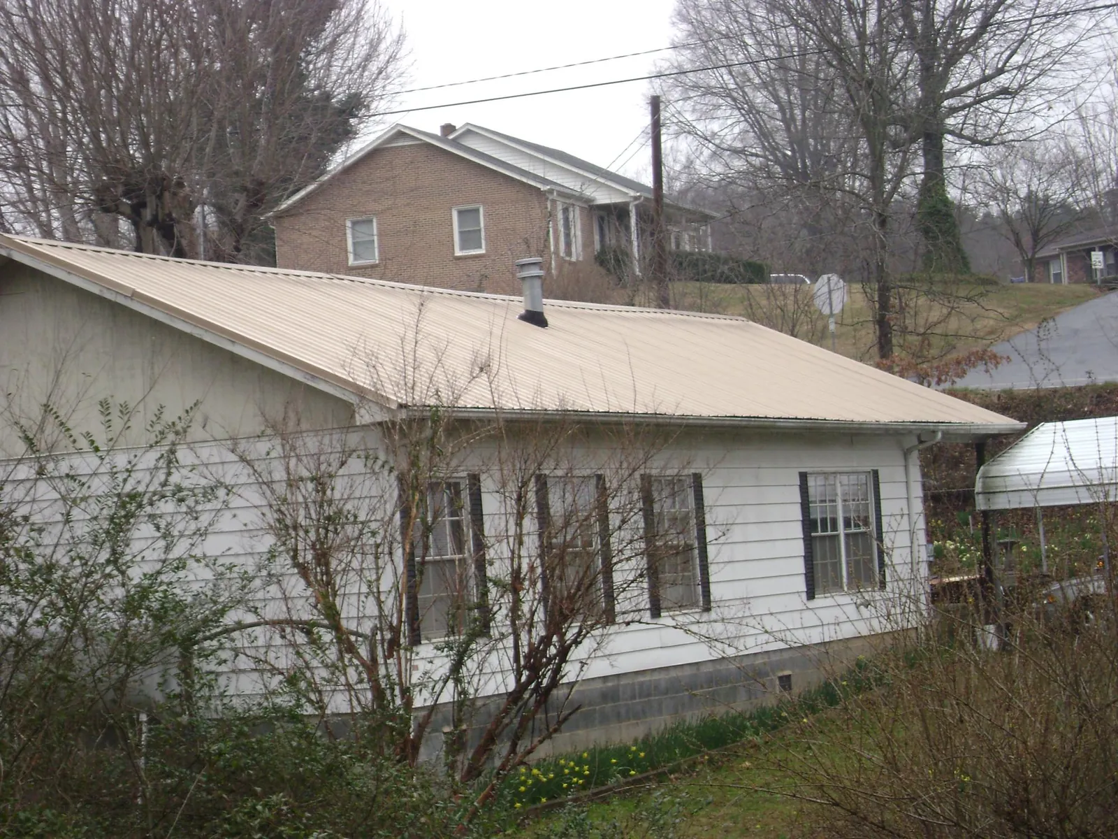 Tan metal roof on a white sided house set into a hillside — Commercial Roofing by Roofing Brothers in Tennessee